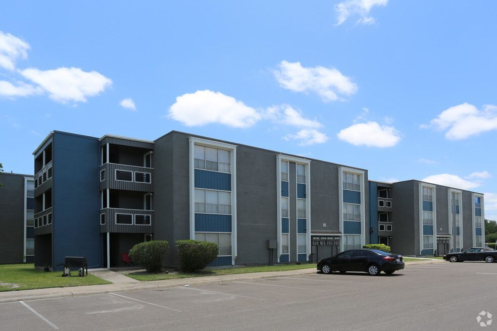 Apartment building with blue and gray exterior, parked cars, and blue sky.