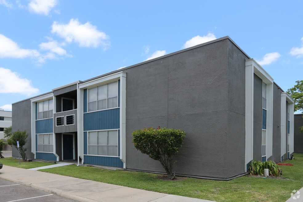 Two-story apartment building with dark gray stucco exterior and teal accents, blue sky.