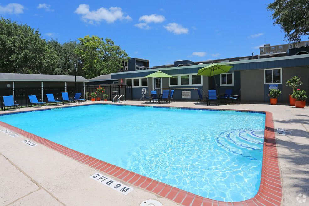 Pool with blue water, lounge chairs, and umbrellas. Building in background. Sunny day.