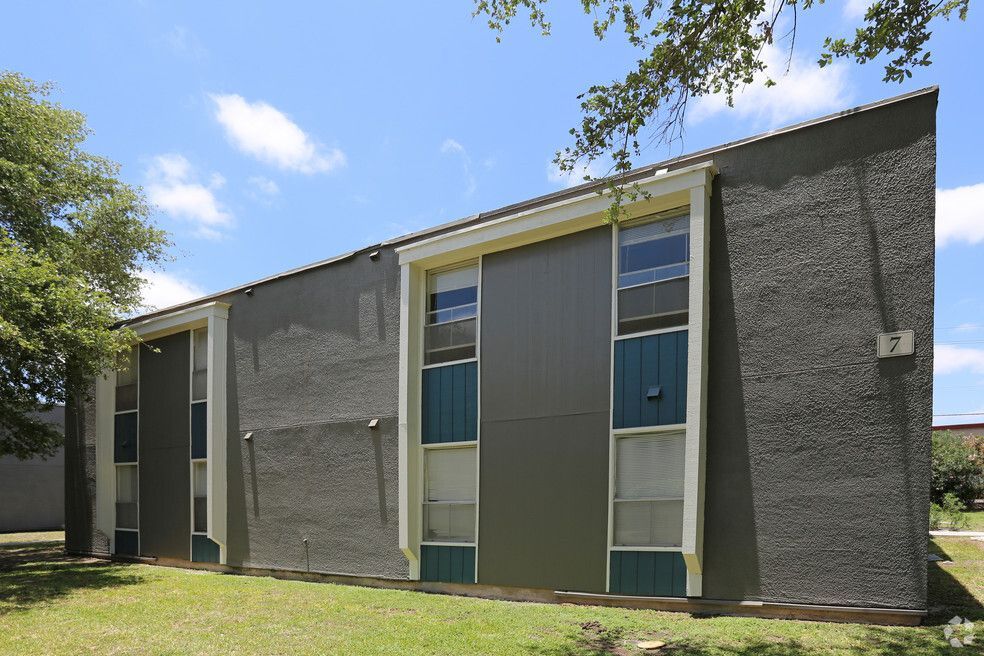 Gray apartment building with teal accents, blue sky, and green grass.