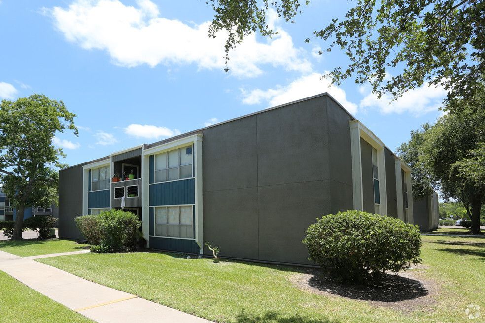 Two-story apartment building with blue and gray exterior, green lawn, sunny day.