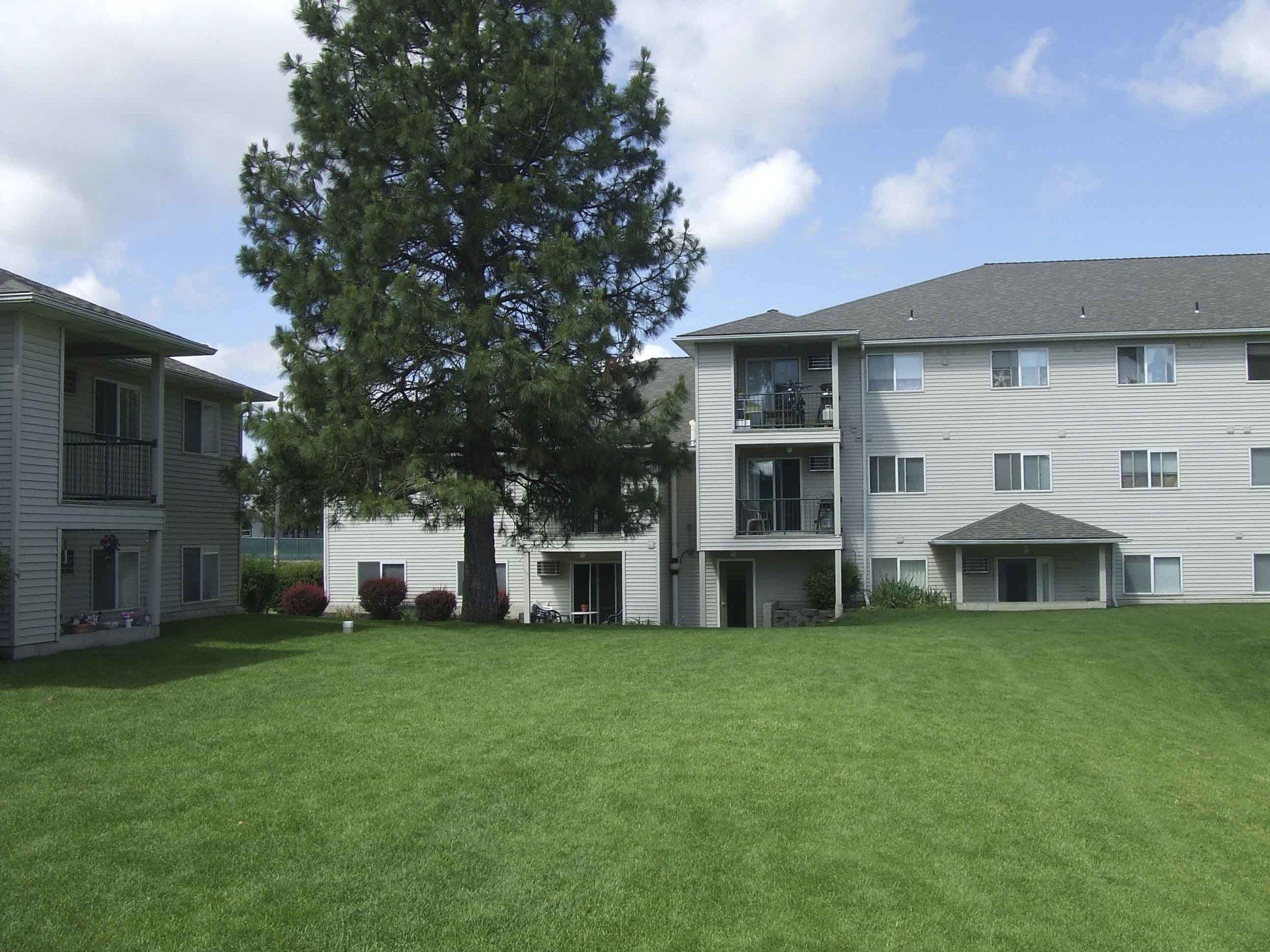 Apartment buildings with green lawn under a partly cloudy sky.