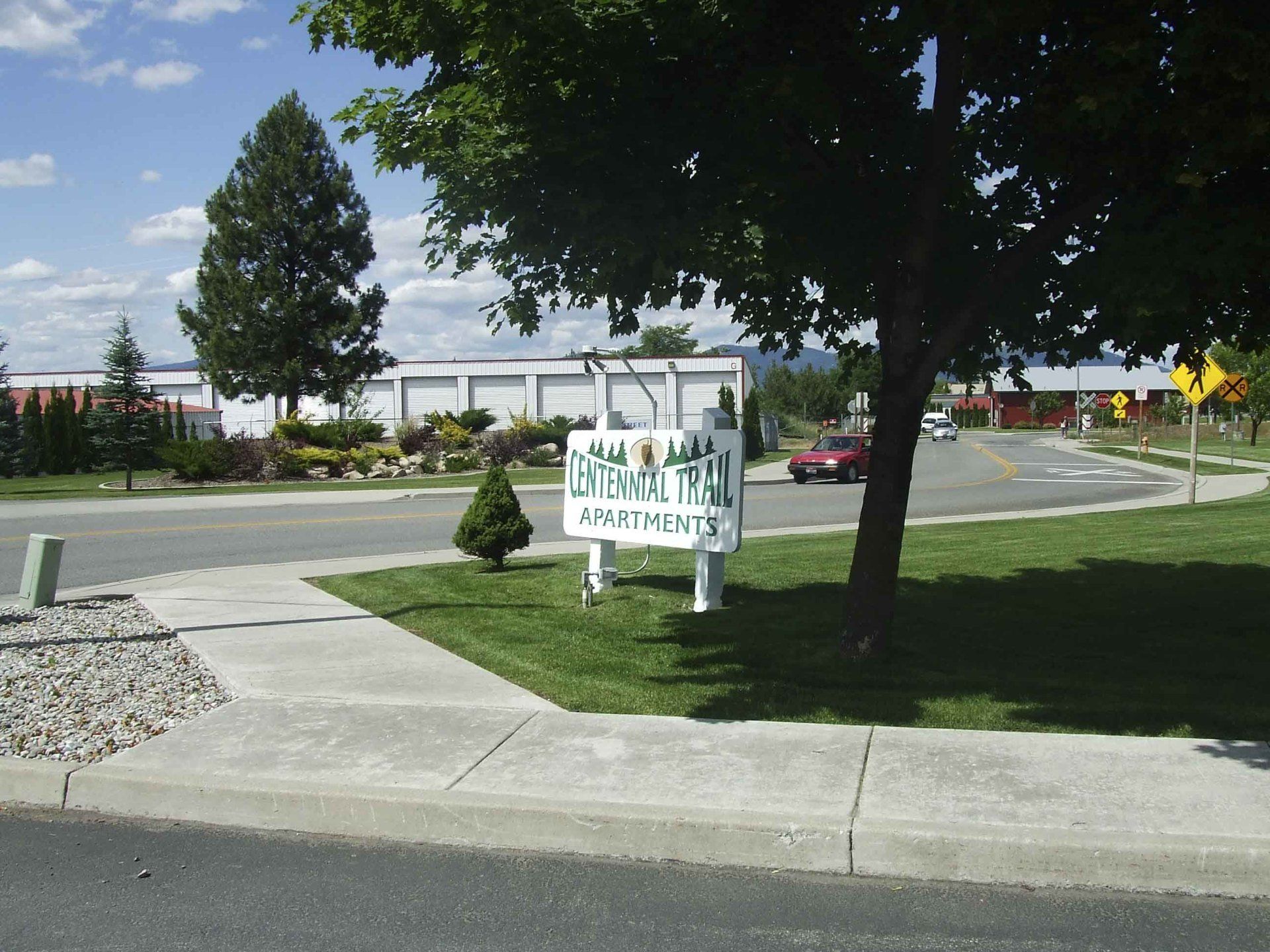 Sign for Aspen Place Apartments near a curved road and trees.