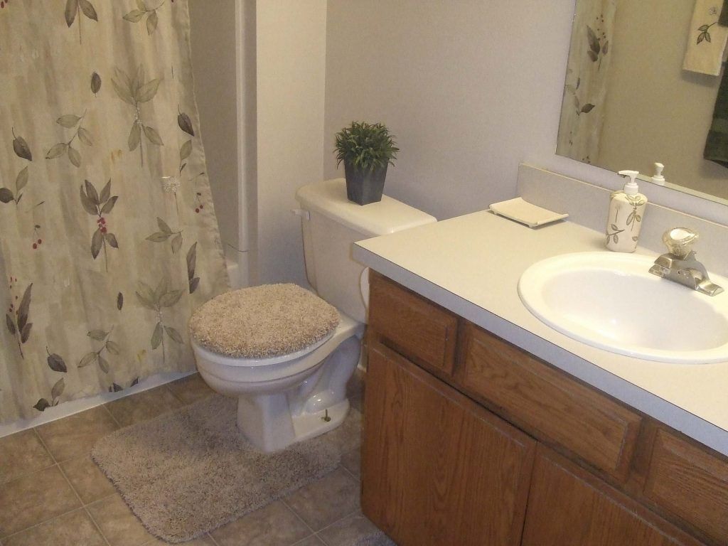 Bathroom with toilet, sink, and shower. Tan countertop, wooden cabinets, and floral shower curtain.
