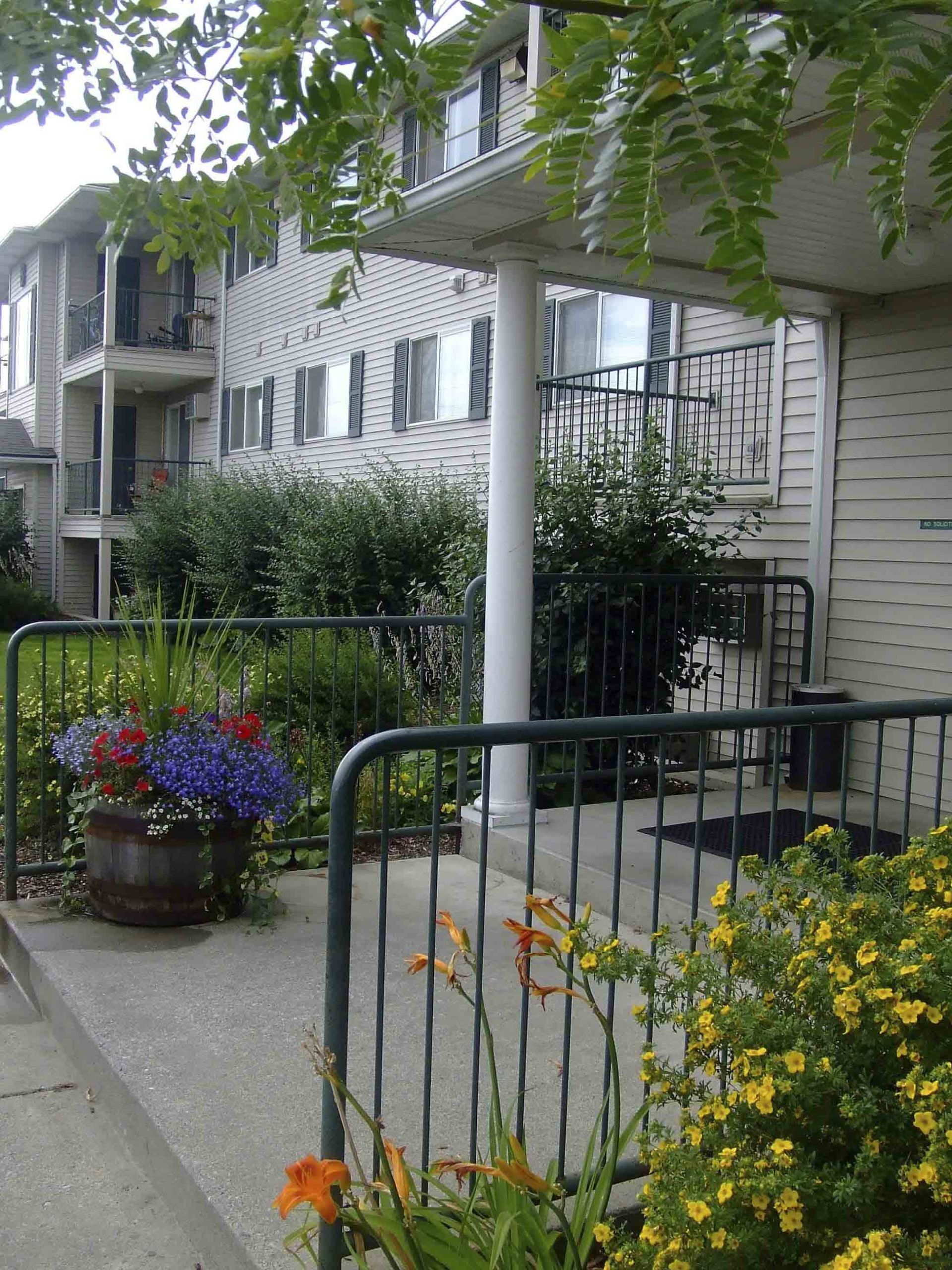 Apartment building exterior with a garden, railings, and flowers.