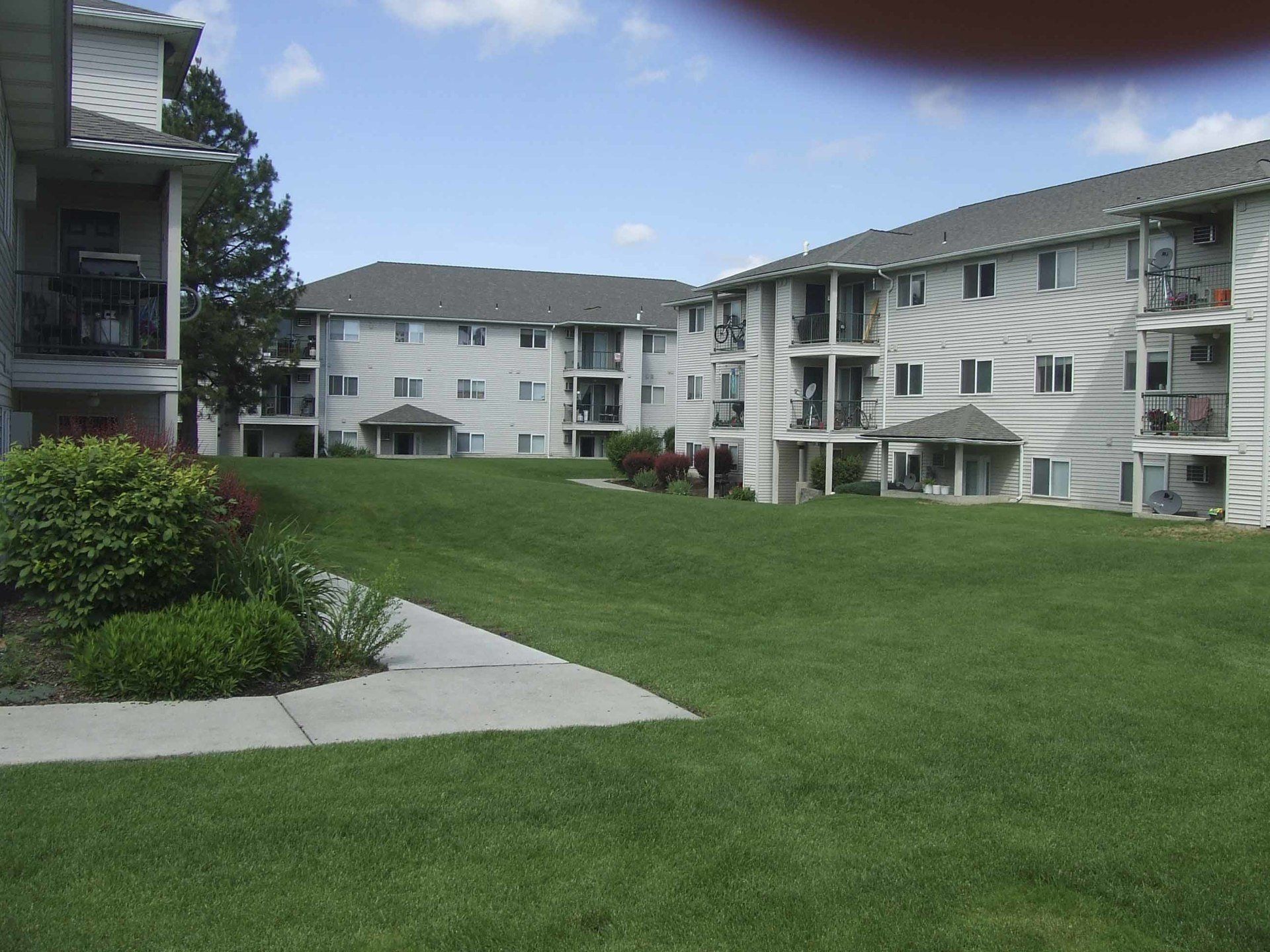 Apartment complex with manicured lawn on a sunny day. White buildings, green grass, and blue sky.