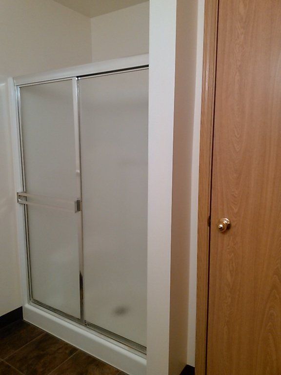 Shower stall with sliding frosted glass doors, next to a wooden door.