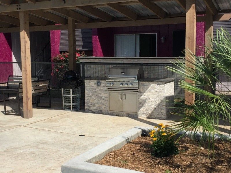 Outdoor kitchen with a grill, bar, and seating under a wooden pergola.