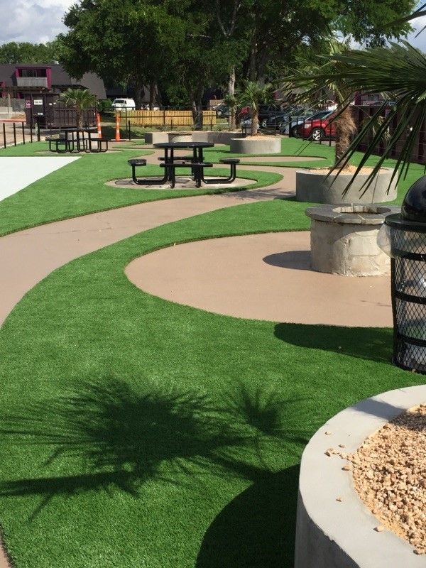 Park with green turf, curved walkways, picnic tables, and concrete seating areas.