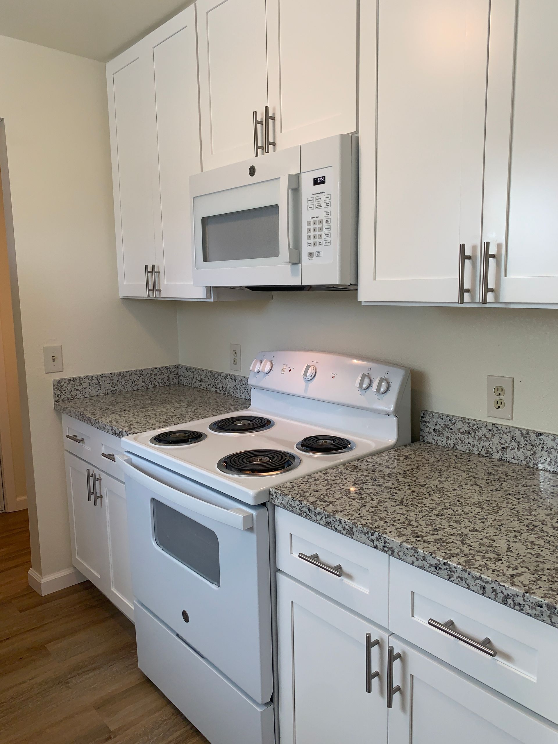 White kitchen with a stove, microwave, countertops, and cabinets.