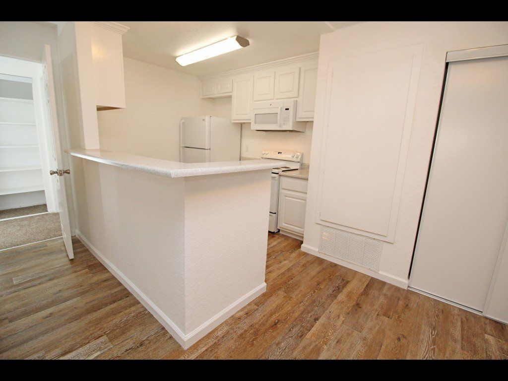 Kitchen with white cabinets and appliances, breakfast bar, and wood-look flooring.