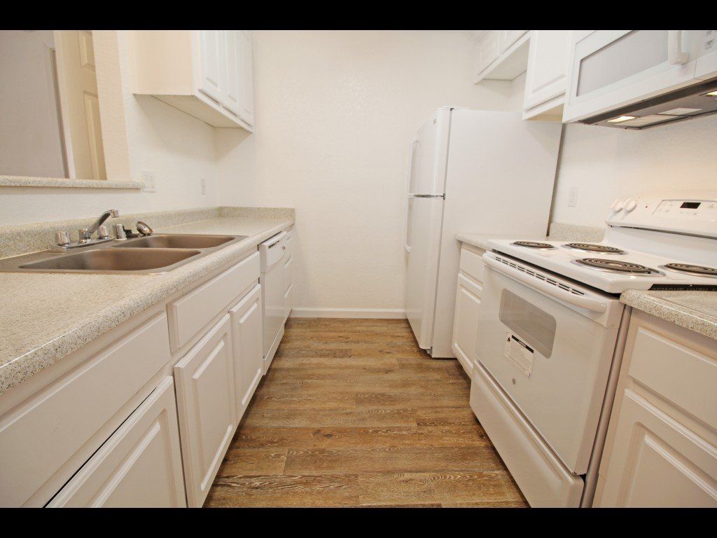 White kitchen with appliances, cabinets, and a sink. Wood-look flooring.