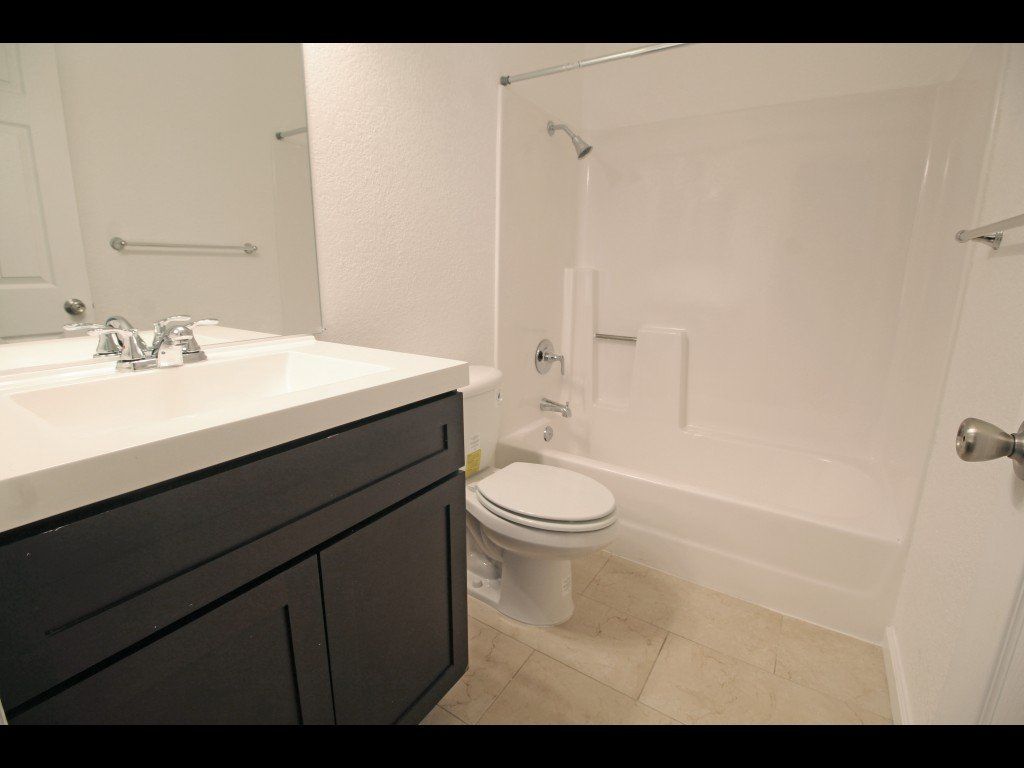 Bathroom with white tub, toilet, and sink with dark cabinet. Light beige floor.