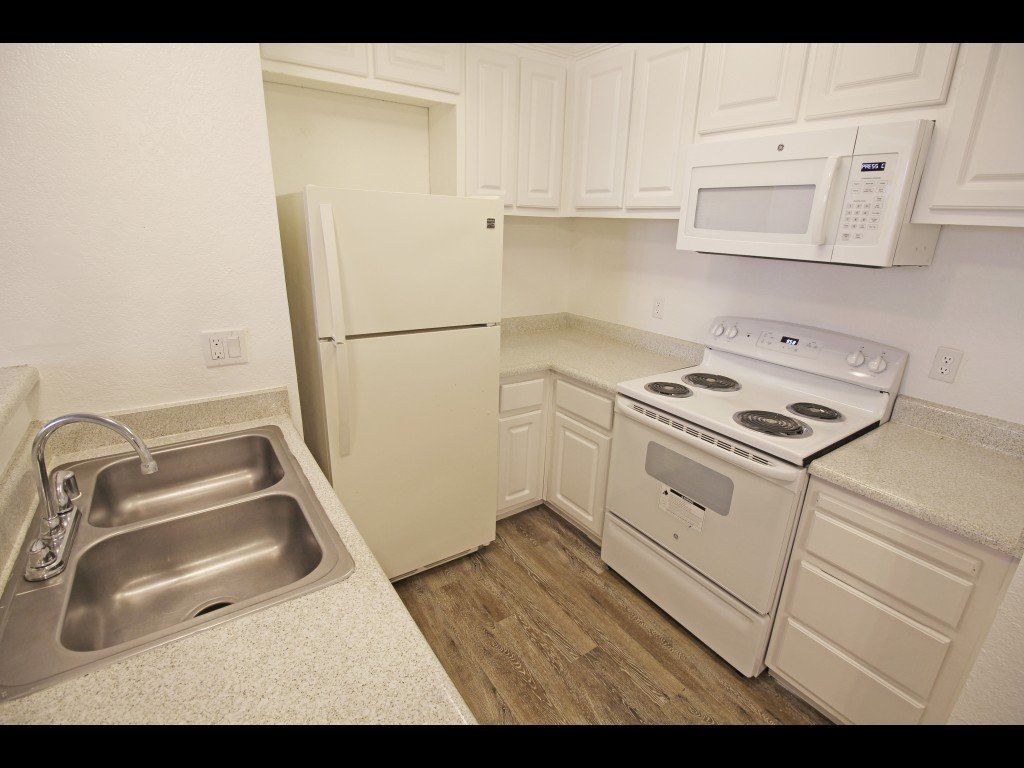 White kitchen with a refrigerator, stove, microwave, and sink.