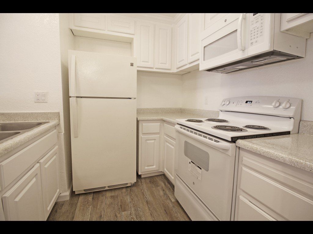 White kitchen with appliances, cabinets, countertops, and wood-look flooring.