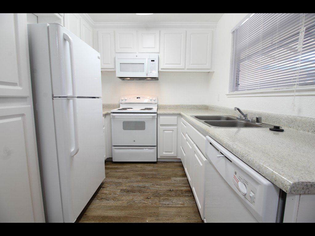 White kitchen with appliances and cabinets, light countertops, and a window.