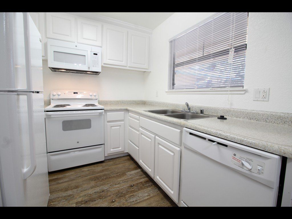 White kitchen with appliances, cabinets, and a window with blinds.