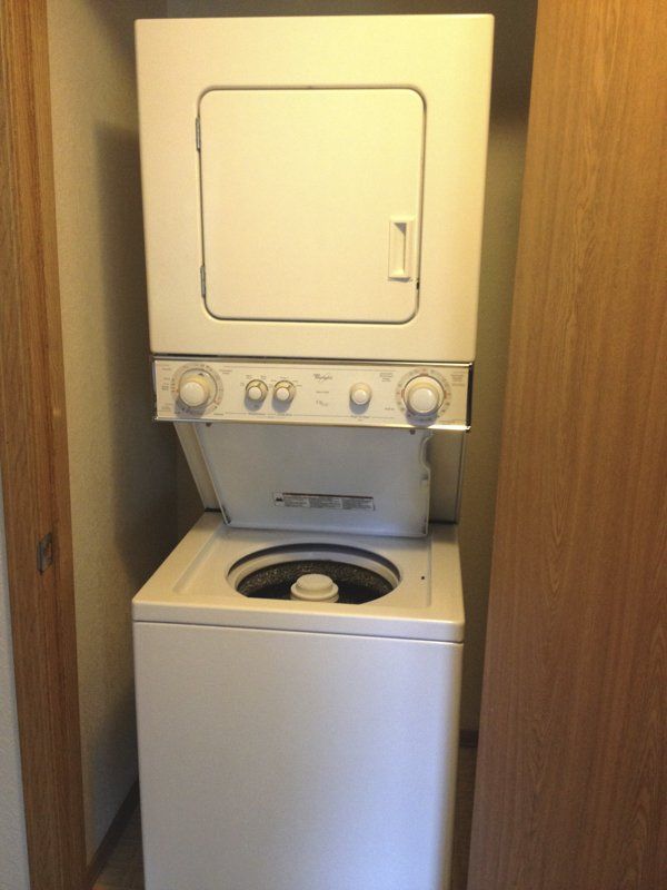 Stacked white washer and dryer units in a narrow closet.