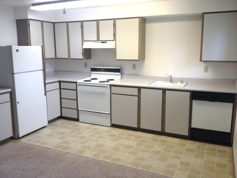 Kitchen with white cabinets, appliances, light countertops, and beige flooring.