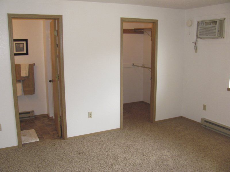 Empty bedroom with brown carpet, two doorways, an air conditioner, and baseboard heaters.
