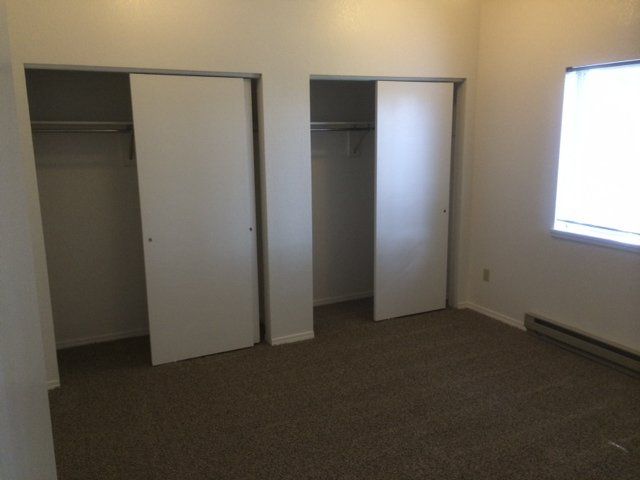 Empty bedroom with two closets and a window. Brown carpet, white walls.