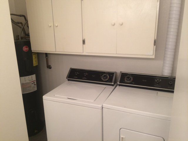 Laundry room with a washing machine, dryer, water heater, and cabinets.
