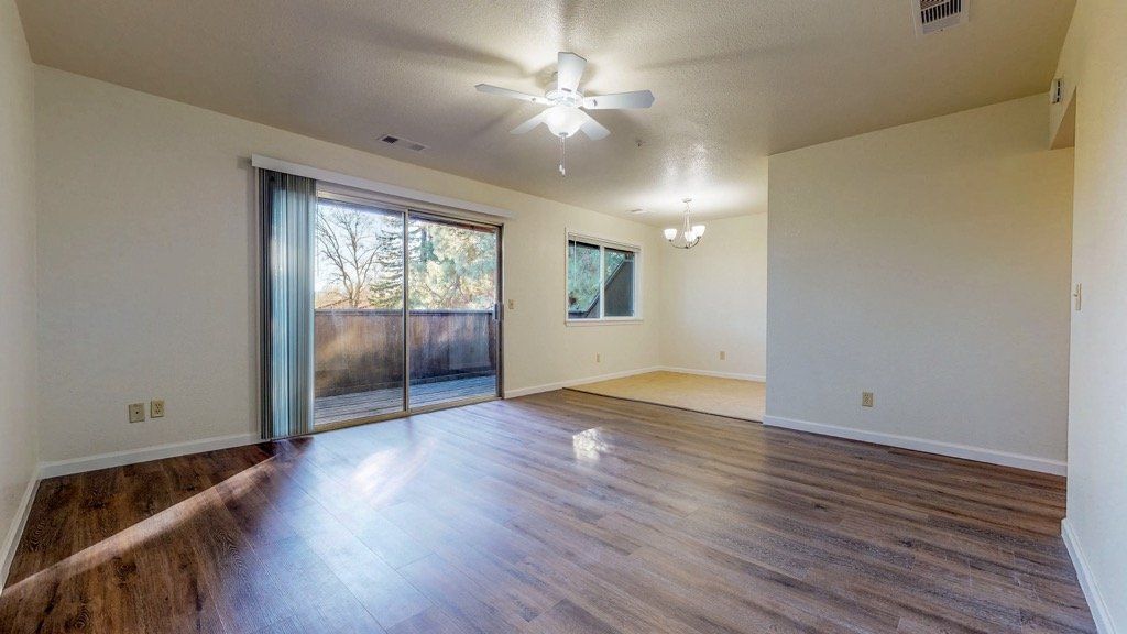 Living room with wood flooring, sliding door to balcony, and a ceiling fan.