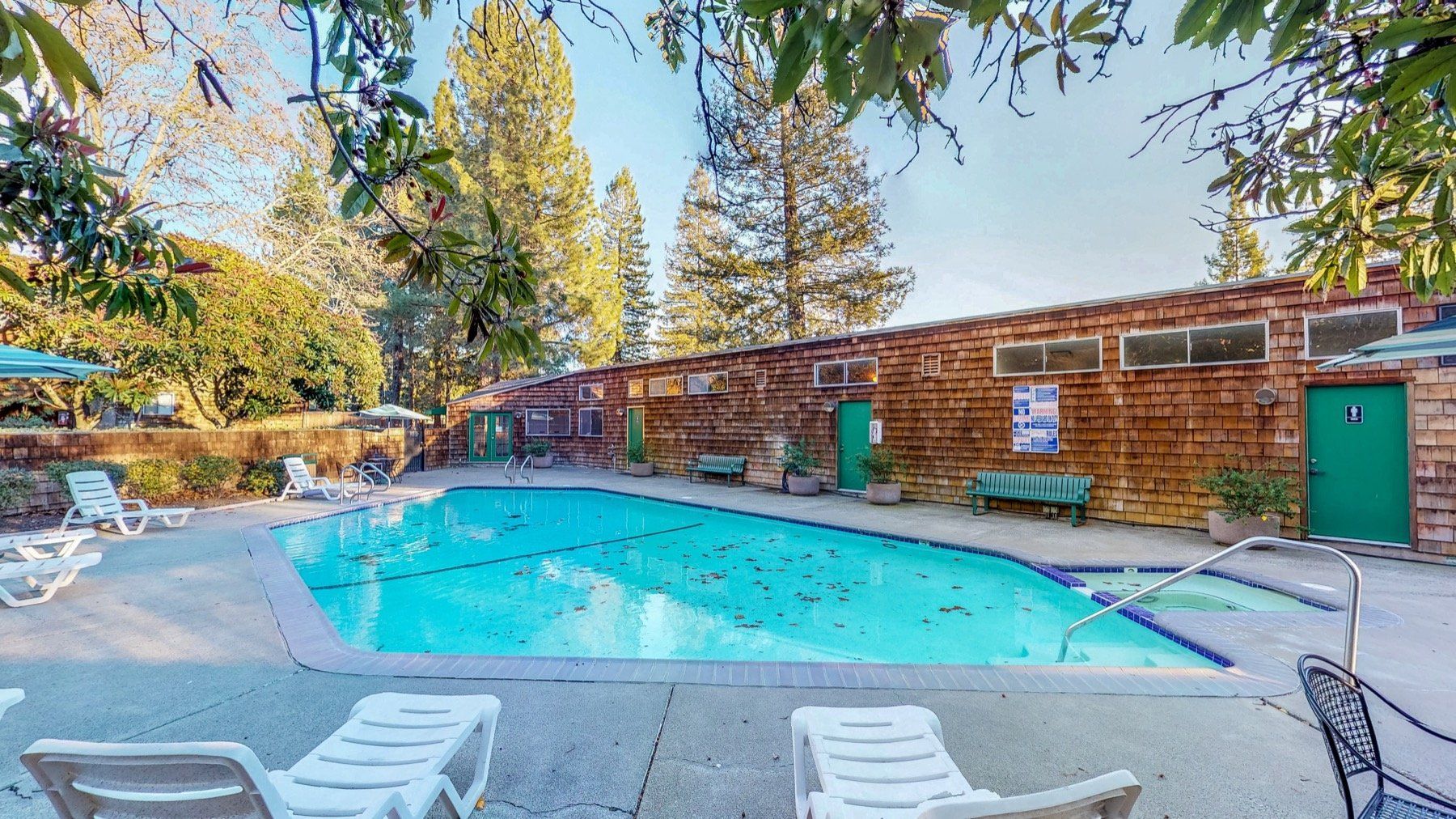 Pool with lounge chairs and a building, outdoors on a sunny day.