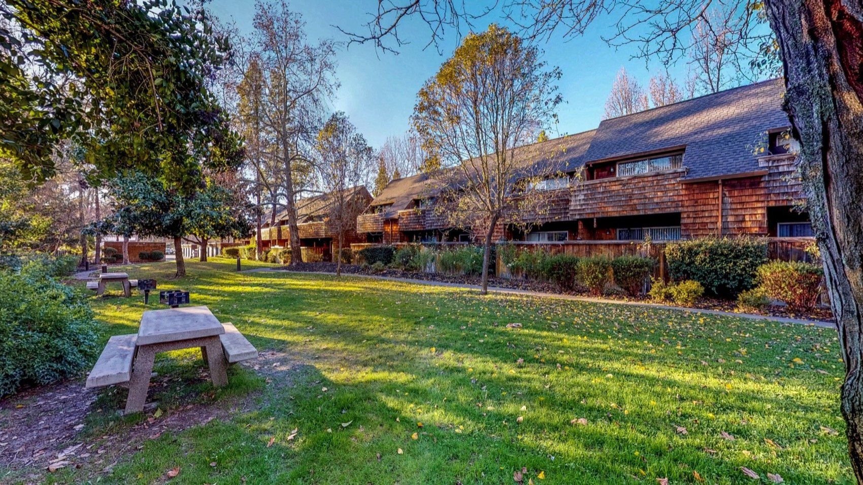 Grassy park with picnic tables in front of wood-sided townhouses under a blue sky.