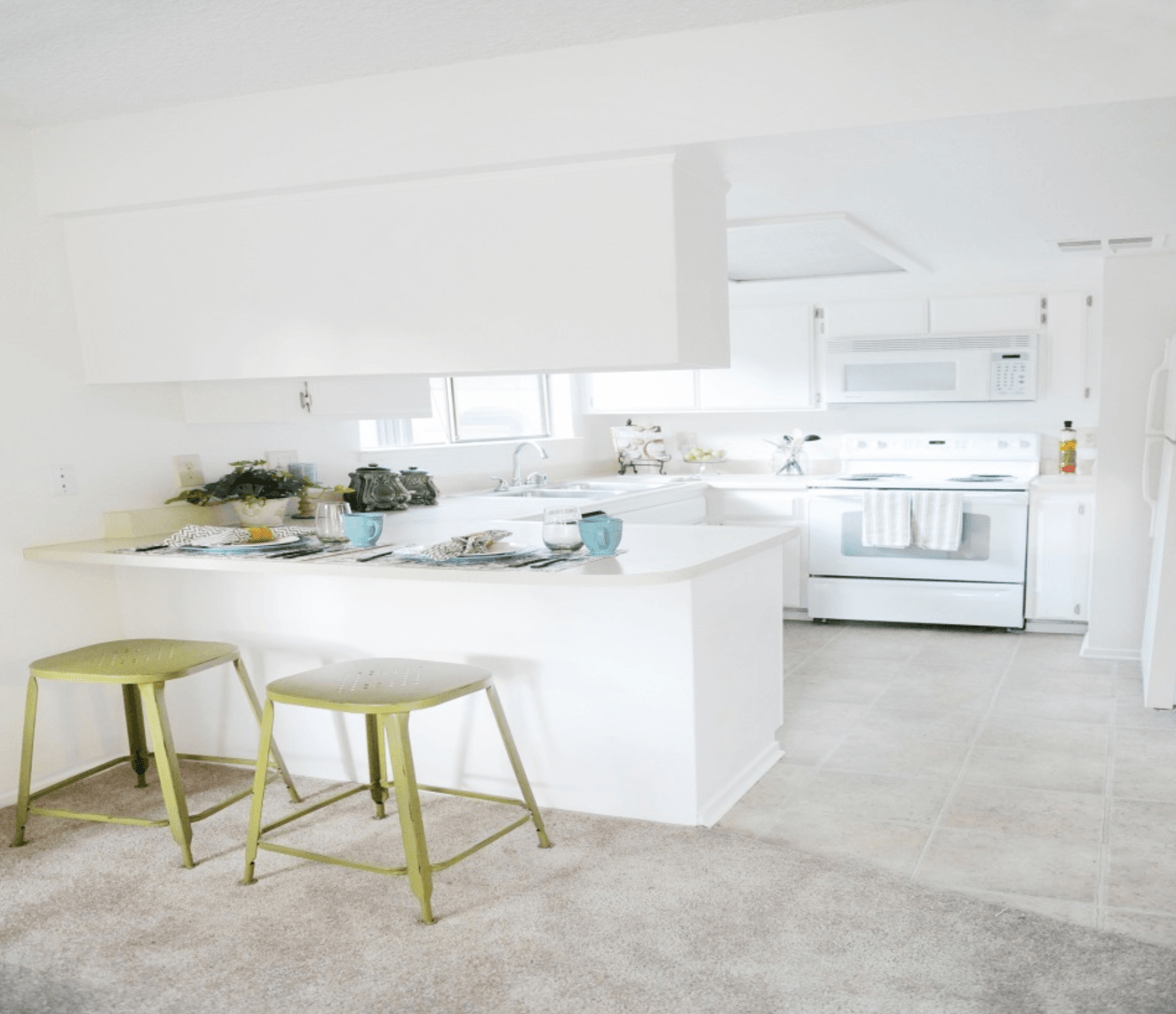 White kitchen with breakfast bar, two green stools, and a microwave and stove.