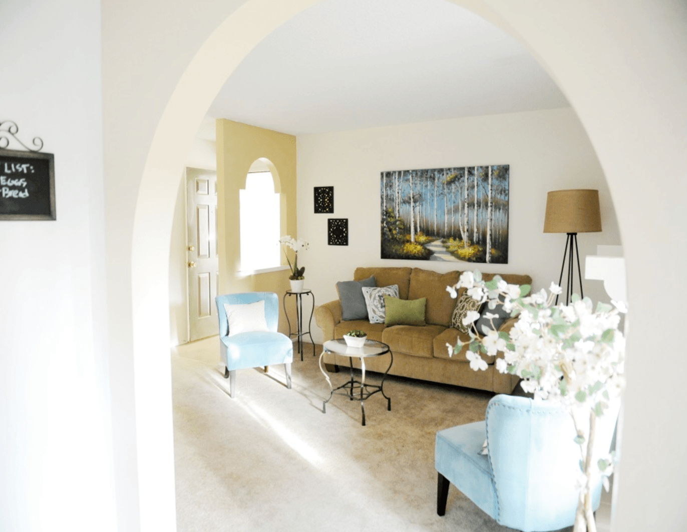 Living room with archway entrance, light blue chairs, brown couch, and landscape art.