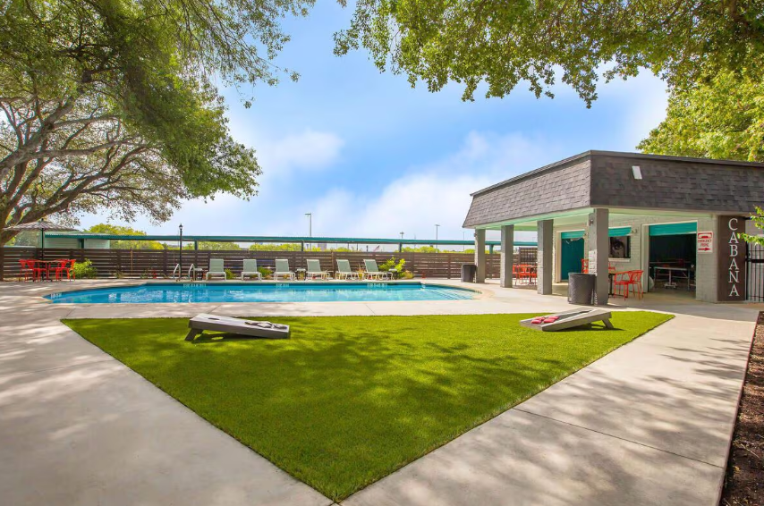 Poolside area with a pool, lounge chairs, and a covered patio under a blue sky.
