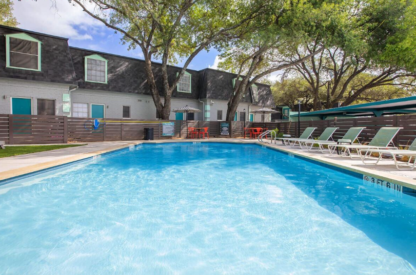 Swimming pool in front of an apartment building with lounge chairs on the side.