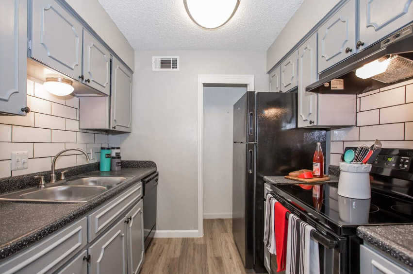 Galley kitchen with gray cabinets, white subway tile, and black appliances.