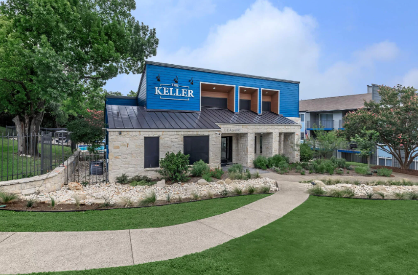 Exterior of the Keller apartment complex. Building with blue facade and stone exterior. Paved walkway and green lawn.