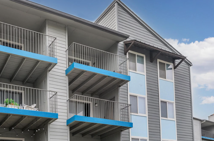 Apartment building exterior with blue balconies and gray siding against a blue sky.