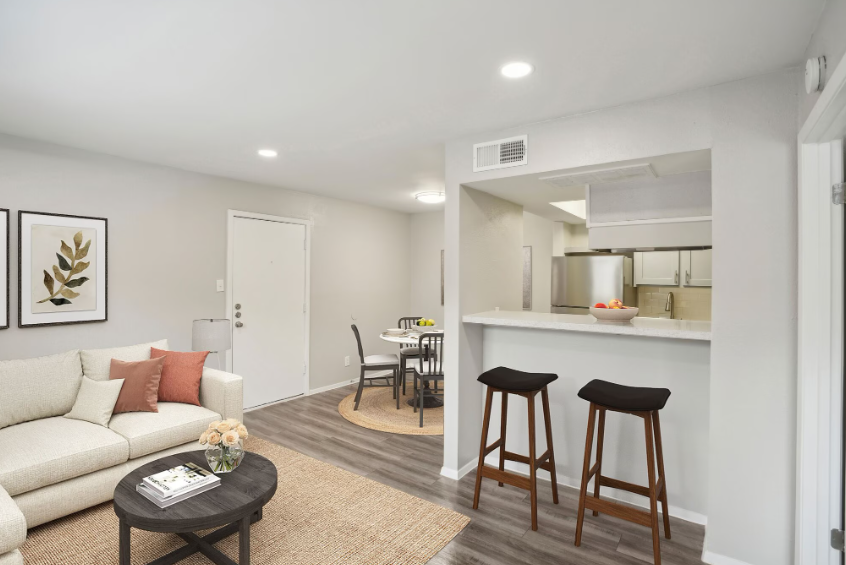 Living room with a white couch, bar stools, and dining table, with a view into the kitchen.