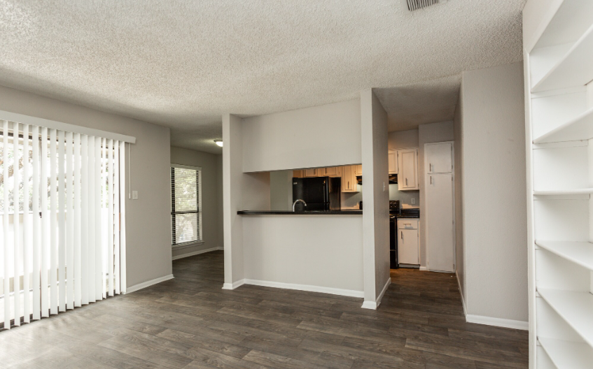 Interior view of an apartment, showing living area with dark wood-look floors, and open kitchen.