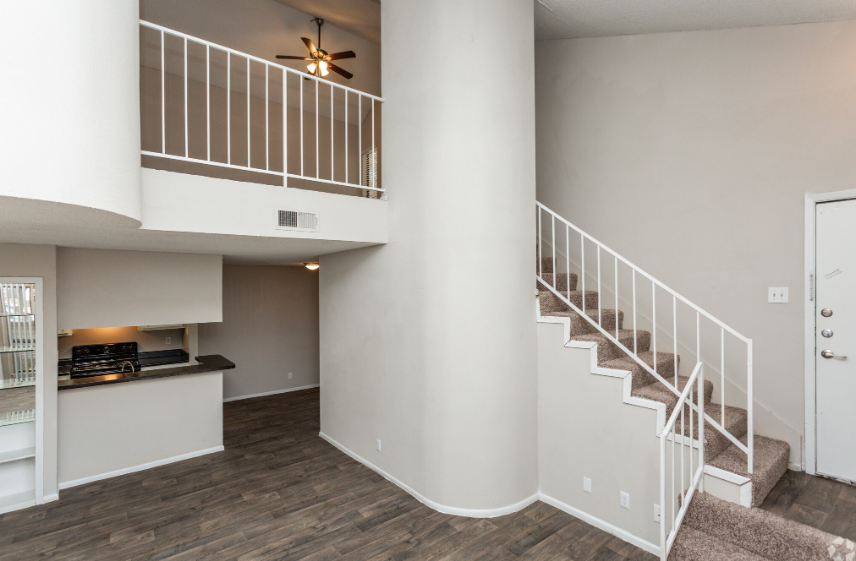 Living room with staircase leading to a loft. Features neutral walls, hardwood floors, and a white railing.