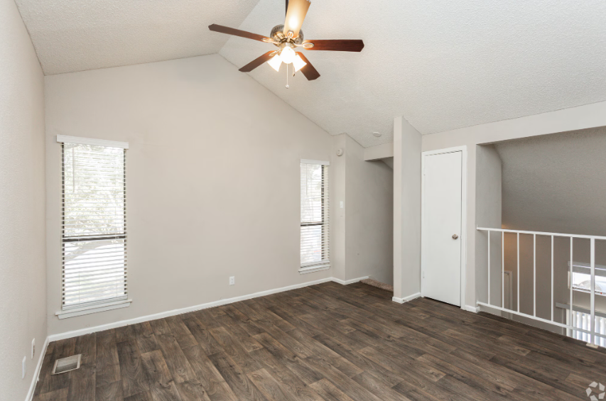 Empty room with vaulted ceiling, two tall windows, ceiling fan, and dark wood-look flooring.