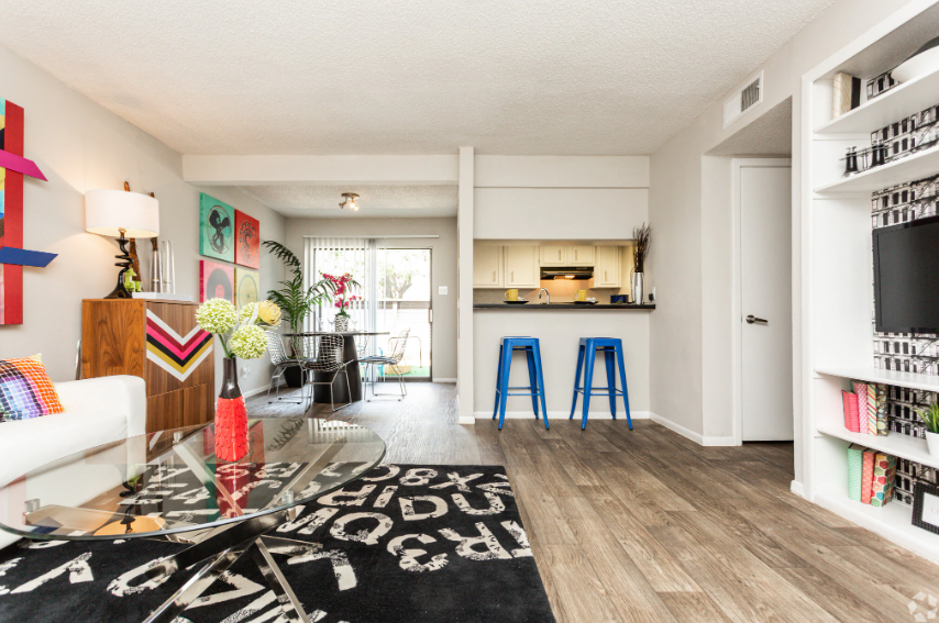 Living room with colorful art, white sofa, glass coffee table, and wood floors.
