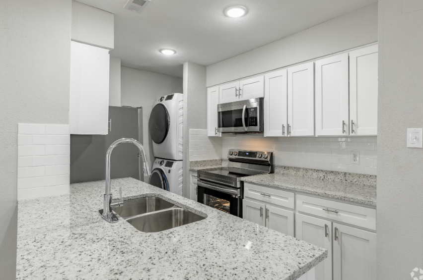 Modern kitchen with white cabinets, granite countertops, and stacked washer/dryer unit.