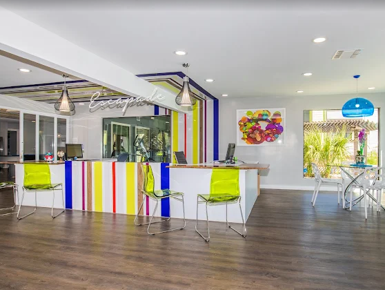 Reception desk with colorful striped front, chairs, artwork, and windows.