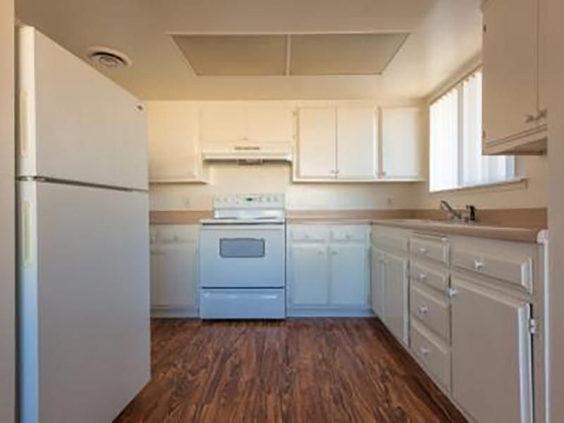White kitchen with white appliances, cabinets, and brown wooden floor.