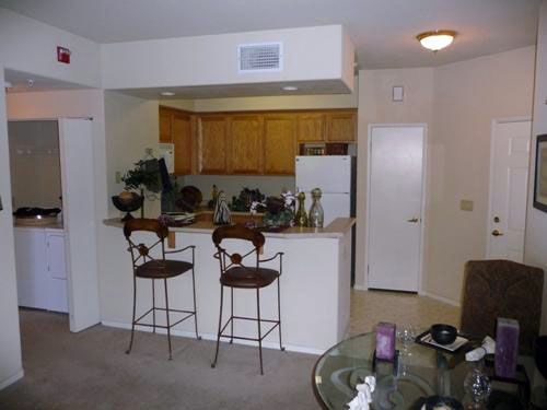 Kitchen with a breakfast bar, two stools, wooden cabinets, and white appliances.