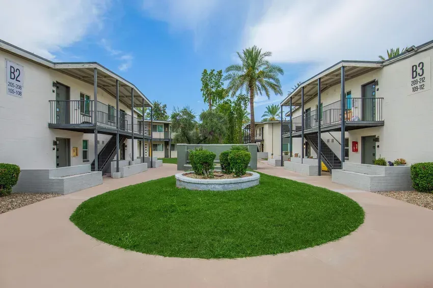 Apartment buildings with balconies around a grassy courtyard with shrubs and a palm tree.