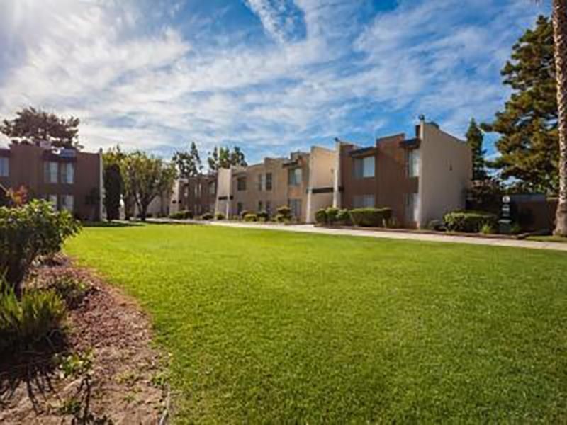 Apartment complex with a large green lawn under a partly cloudy blue sky.
