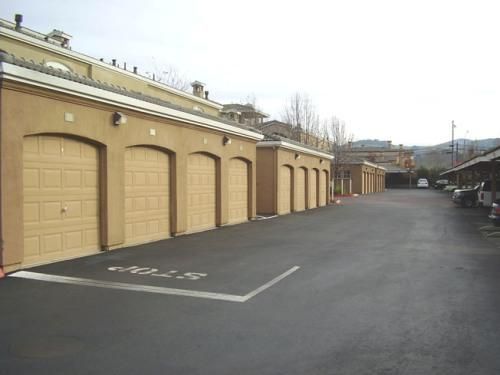 Row of tan garage doors in an apartment complex with black asphalt road. Stop sign painted on road.