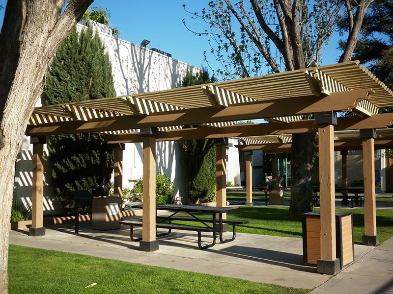 A park shelter with a picnic table and trash can on a sunny day.
