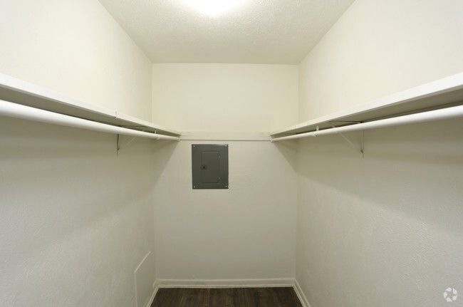 Empty walk-in closet with white walls, shelves, and a gray electrical panel. Dark wood-look floor.